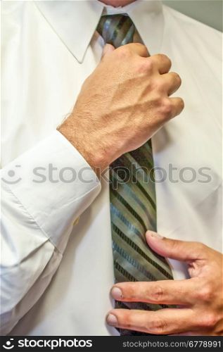 man fixing a tie with hands in white shirt