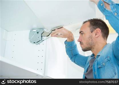 man fixing hanging cabinet door mechanism