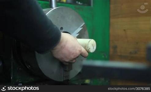 Man fixing workpiece in headstock of turning lathe machine for cutting and drilling work in workshop