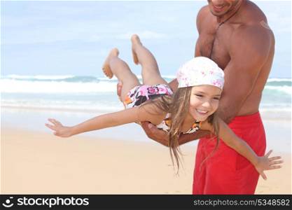 Man flying his daughter around a beach