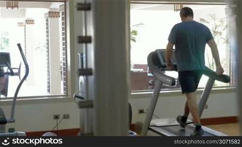 Man getting cardio training on treadmill. He walking on exercise machine in modern gymnasium
