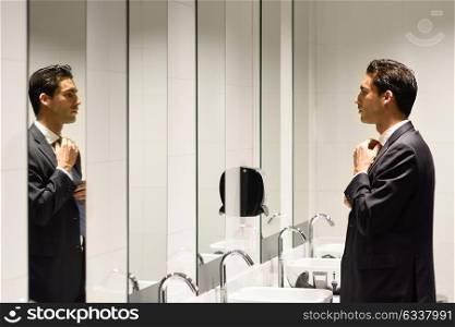 Man getting dressed in a public restroom with mirror. Businessman wearing suit and tie.