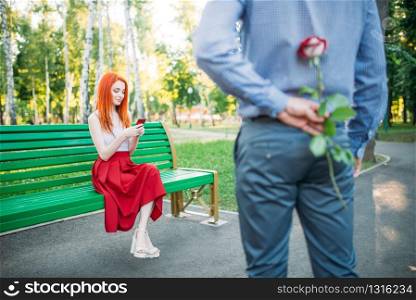 Man gives woman flower, romantic date of couple on a bench in summer park. Man gives woman flower, romantic date