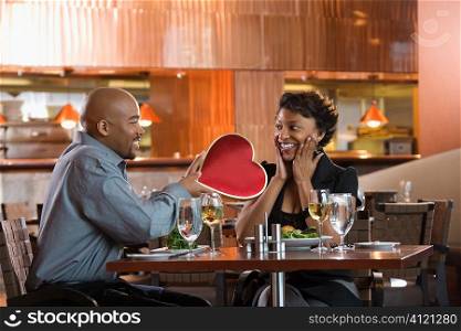 Man Giving Woman Heart Shaped Box at Restaurant