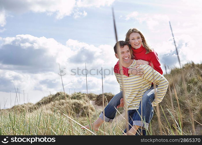 Man giving woman piggy back on dunes