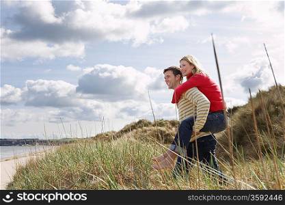 Man giving woman piggy back on dunes