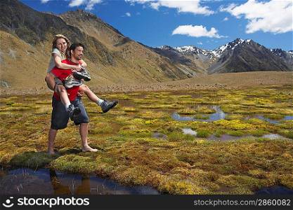 Man giving woman piggy-back ride through pond near mountains
