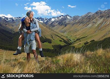 Man giving woman piggy-back ride up hill with mountains behind