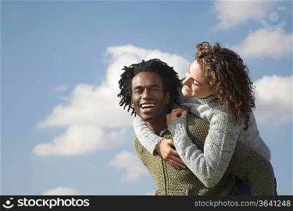 Man giving woman piggyback against sky