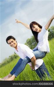 Man giving woman piggyback in meadow, laughing. Narrow focus on his eye.