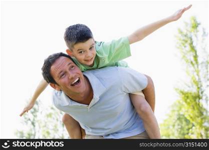 Man giving young boy piggyback ride outdoors smiling