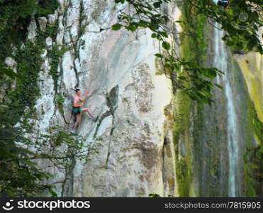 Man going up on the rocks and waterfall by rope