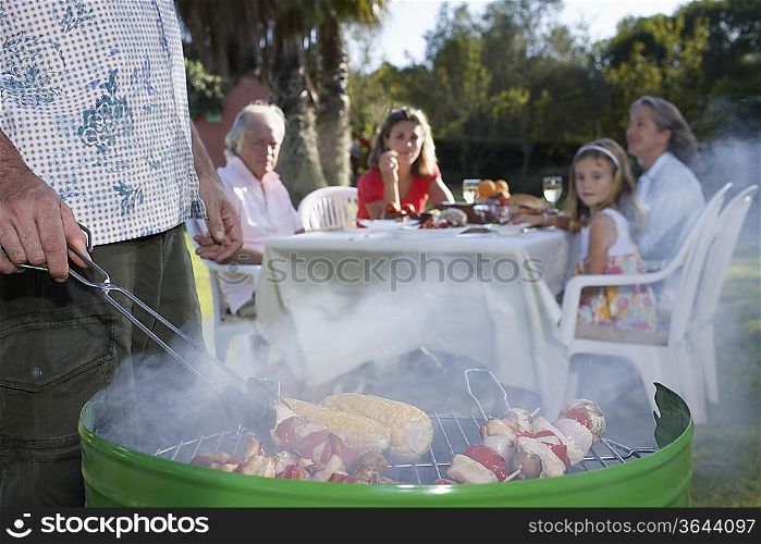 Man grilling, other family members sitting at table in background, close-up