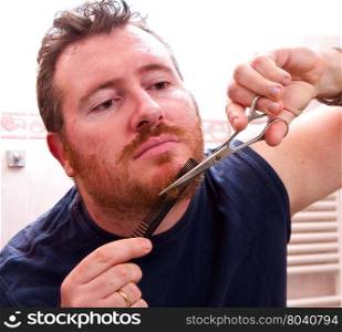 man grooming his beard with scissors