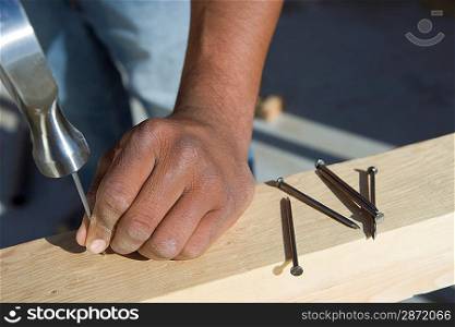 Man hammering nails to wooden plank