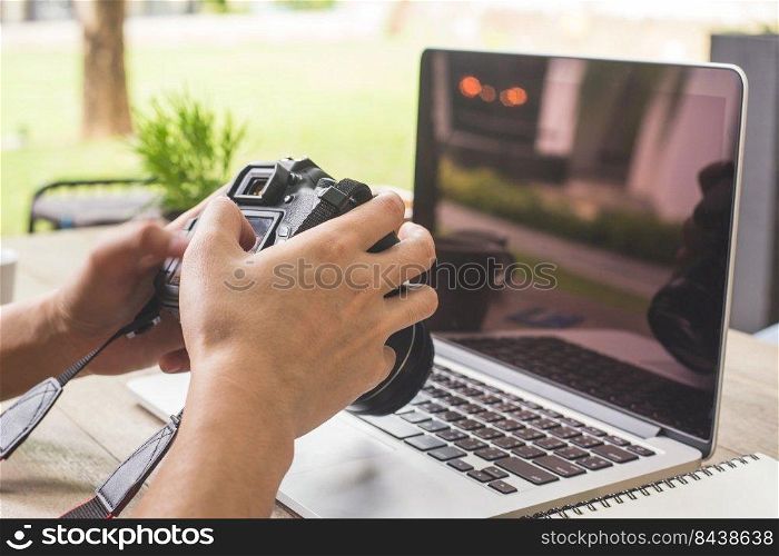 Man hand holding camera and using laptop computer in coffee shop.