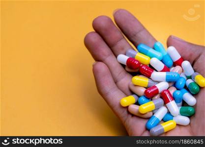 Man hand holding colorful capsule pills on yellow background. Prescription drugs. Drug overuse and polypharmacy concept. Drug allergy. Pharmaceutical industry. Pharmacy banner. Healthcare and medicine