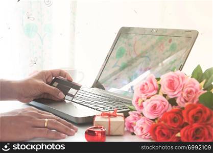 Man hand holding credit card and using computer with gift and rose on table, Shopping online. Valentine&rsquo;s Day concept