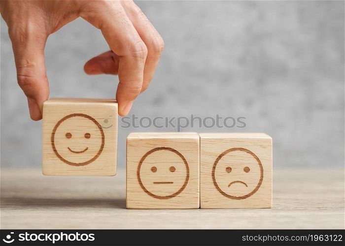 Man hand holding emotion face block. Customer choose Emoticon for user reviews. Service rating, ranking, customer review, satisfaction, mood, evaluation and feedback concept