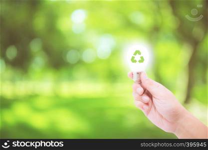 Man hand holding glowing light bulb with recycle symbol on nature background - save energy concept and environment friendly concept.