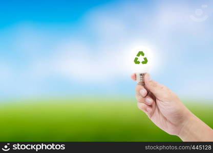 Man hand holding glowing light bulb with recycle symbol on nature background - save energy concept and environment friendly concept.