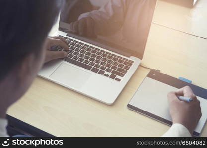 man' hand holding pen working on digital tablet and computer notebook for graphic design work, vintage tone