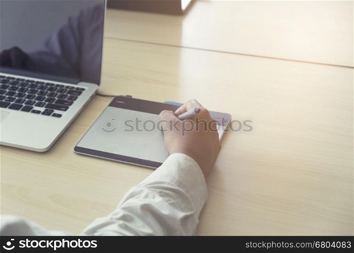 man' hand holding pen working on digital tablet and computer notebook for graphic design work, vintage tone