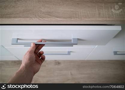 Man hand opening white drawer for cutlery, focus on steel handle of kitchen counter. man hand opening white dishwasher on the kithen