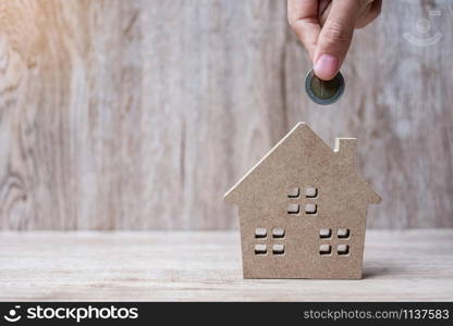 Man hand putting coin over house model on wooden background. Banking, real estate, investment, success, financial and savings concepts