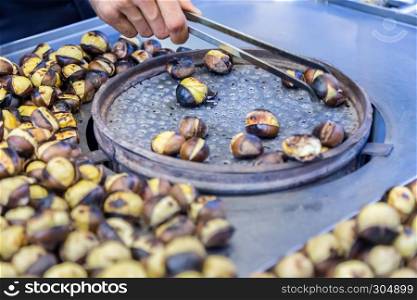 Man hand turns Many Grilled,roasted chestnuts with tongs for sale on a stall. Many Grilled, roasted chestnuts for sale