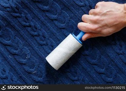 Man hand using a sticky roller to clean fabrics - woolen knitted sweater from dust, hair, lint and fluff, top view, close up.