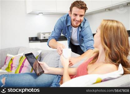 Man Handing Woman Drink As She Uses Digital Tablet At Home