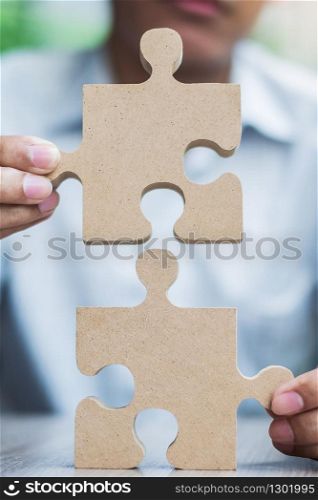 man hands connecting couple puzzle over table, businessman holding wood jigsaw inside office. Business solutions, mission, target, success, goals and strategy concepts