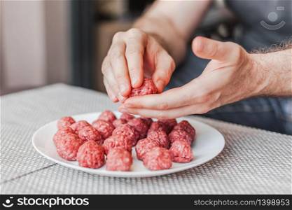 Man hands preparing meatballs with raw mincemeat. Lifestyle close up composition with natural light. Homemade cooking during lockdown, stay home housekeeping sharing concept. Side view with copy space