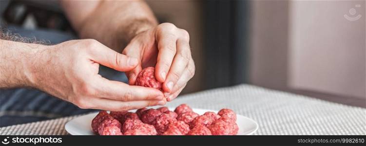 Man hands preparing meatballs with raw mincemeat. Lifestyle close up composition with natural light. Homemade cooking during lockdown, stay home housekeeping sharing concept. Side view with copy space