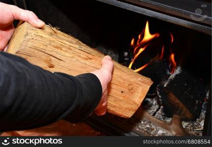 Man hands putting the log to the burning fireplace. Man stoking the wood into fireplace.