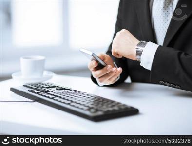 man hands with keyboard watching time and holding smartphone