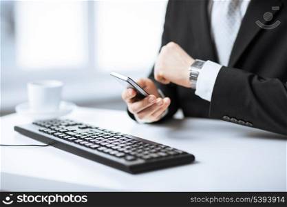 man hands with keyboard watching time and holding smartphone