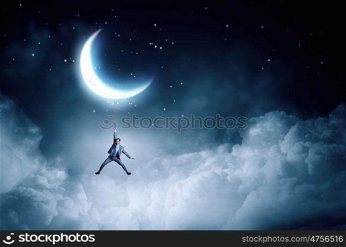 Man hang on moon. Young businessman hanging on rope at night