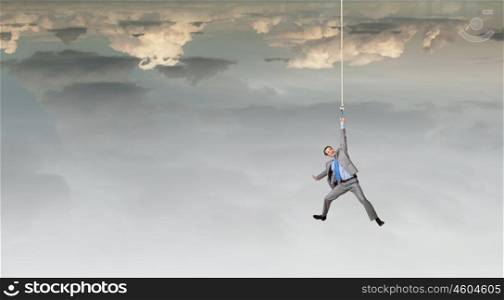 Man hang on rope. Young businessman hanging on rope high in sky