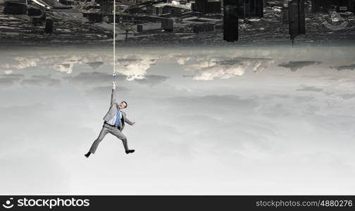 Man hang on rope. Young businessman hanging on rope high in sky