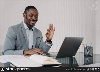 Man has video call on laptop and gestures ok. Teacher is working online at home office and has lesson in sign language. Remote african worker in formal wear in front of camera. E-learning concept.. African teacher working online at home office and has lesson in sign language. E-learning concept.
