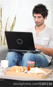 Man having breakfast whilst using laptop