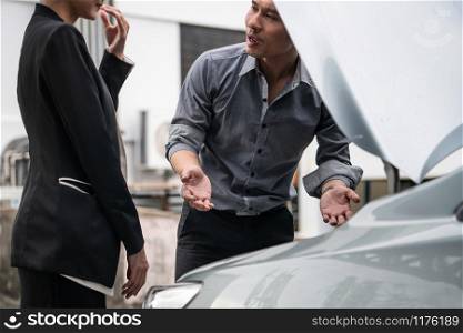 Man help woman fix the car problem. He pop up the car hood to repair the damaged part.