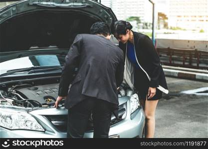 Man help woman fix the car problem. He pop up the car hood to repair the damaged part.