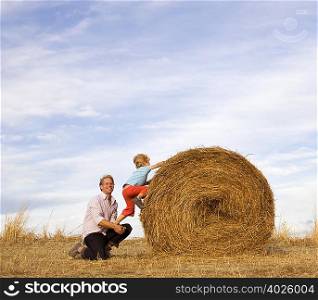 man helping boy to climb hay bale