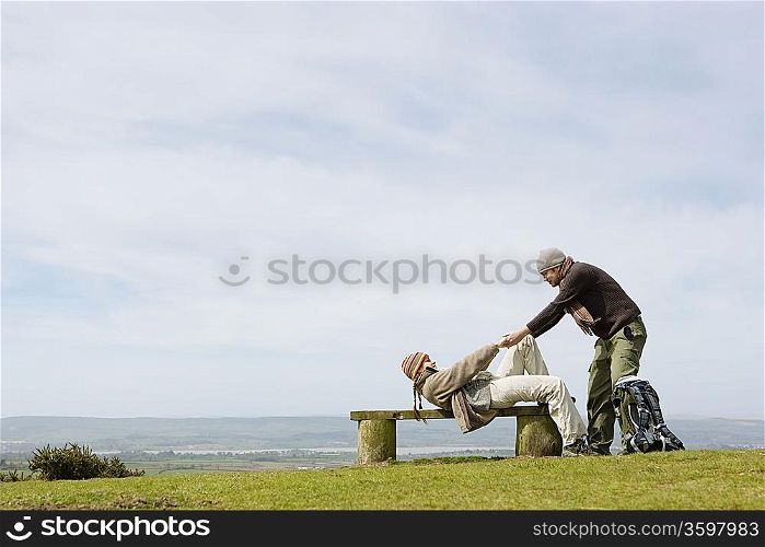 Man Helping Girlfriend up from a Park Bench