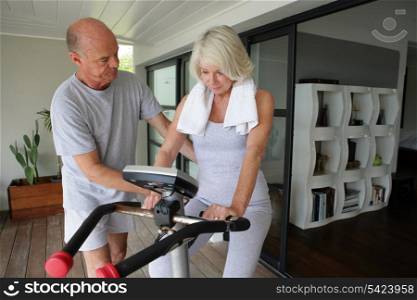 Man helping his wife use an exercise machine
