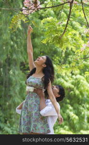 Man helping woman reach for branch of tree