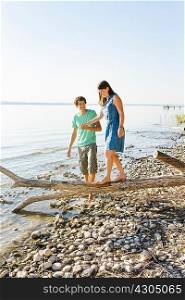 Man helping woman to balance on driftwood, holding hands, Schondorf, Ammersee, Bavaria, Germany